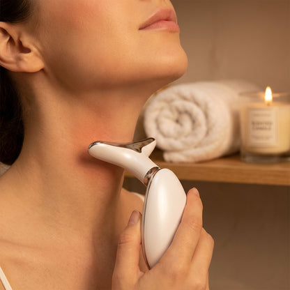 Woman using a white electronic device on her neck with a blurred background of a shelf with towels and a candle.